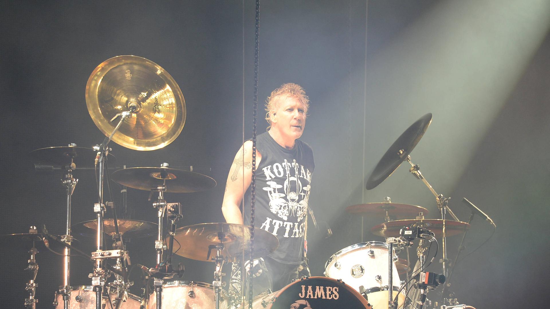 Scorpions-Drummer James Kottak steht mit entschlossenem Gesicht hinter seinem Schlagzeug. Auf seinem T-Shirt steht Kottak-Attack.