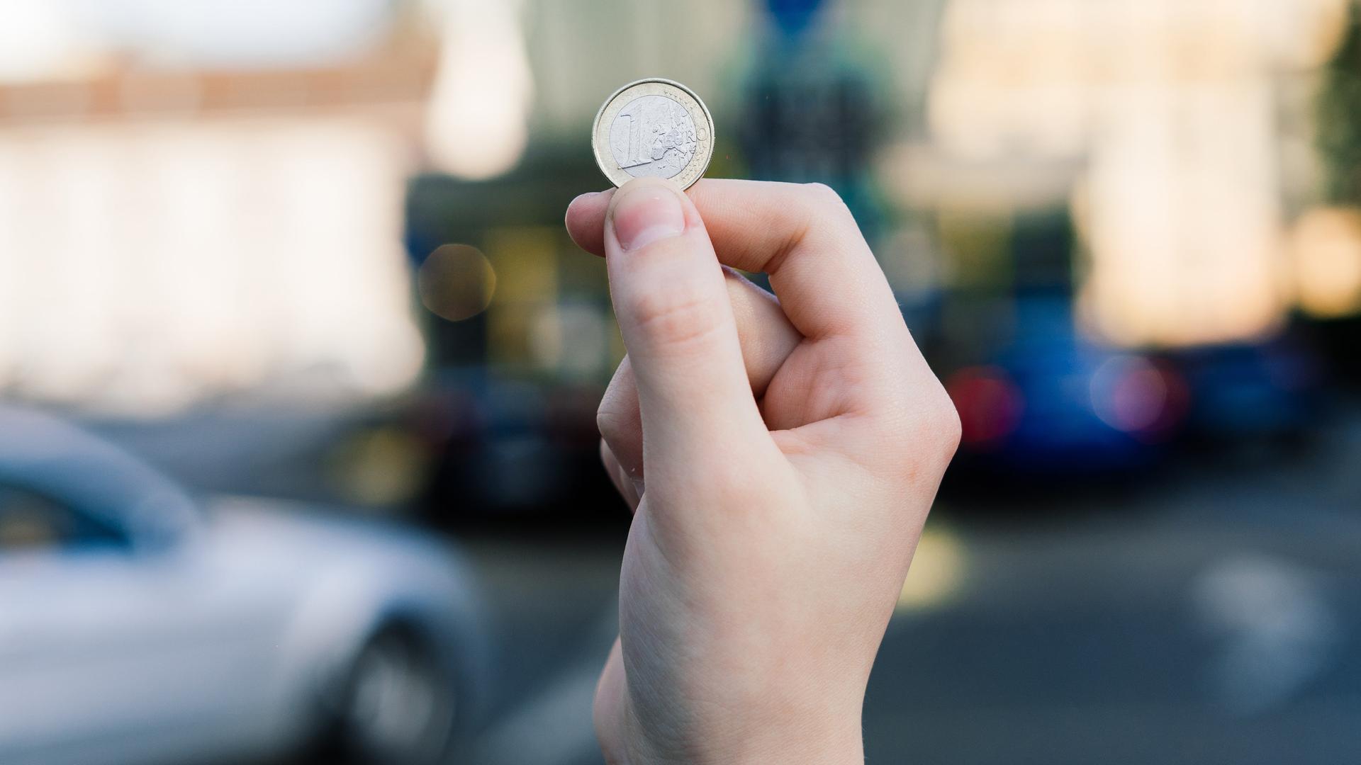 Ein Mann hält eine Euro-Münze in der Luft.