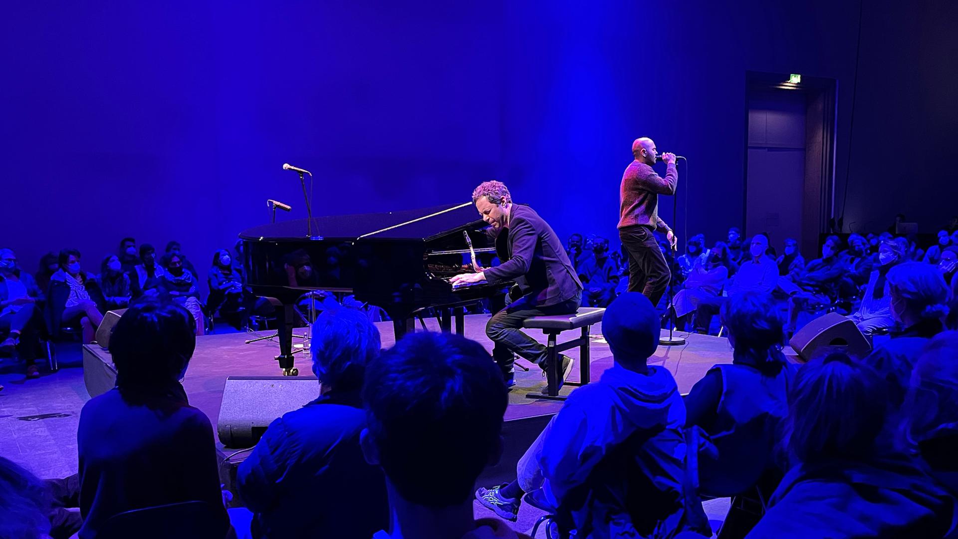Musiker und Publikum sind auf einer Bühne in blaues Licht getaucht