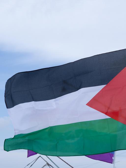 Die Palästinensische Flagge weht an einem Mast. Sie ist horizontal in den panarabischen Farben Schwarz, Weiß und Grün unterteilt. An der linken Seite ist ein rotes Dreieck.