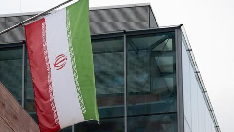 Zu sehen ist ein Gebäude in Frankfurt am Main. Im Vordergrund die iranische Flagge.