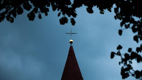 Das Kreuz einer katholischen Kirche vor einem dunklen Abendhimmel