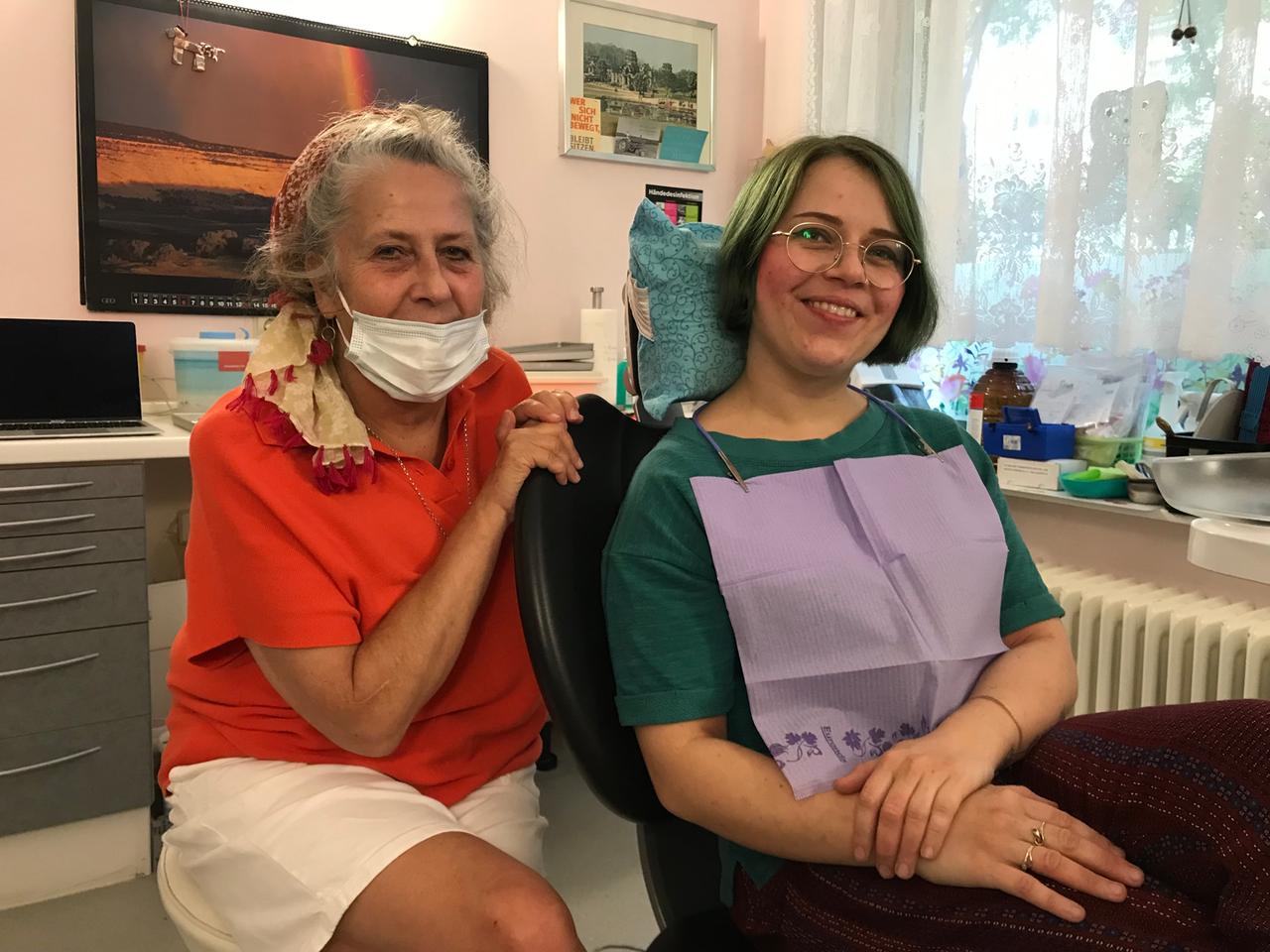 Ute Stein und eine auf dem Zahnarztstuhl sitzende Patientin lachen in die Kamera.