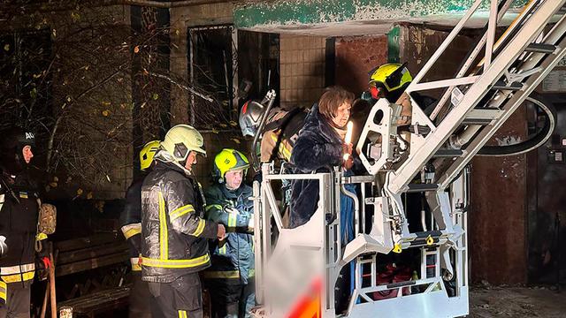Ukrainische Feuerwehr-Leute bringen Menschen aus einem Wohn-Haus in Sicherheit. 