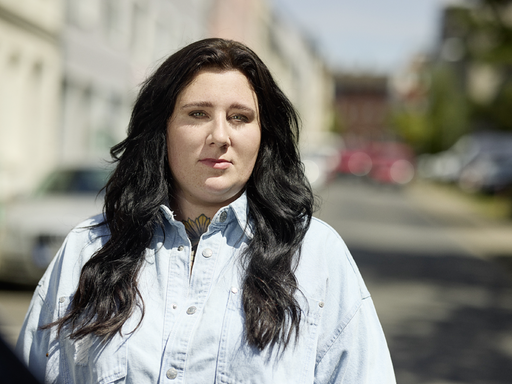 Porträt von Lena Schätte. Sie hat langes, welliges schwarzes Haar und trägt ein Jeanshemd.