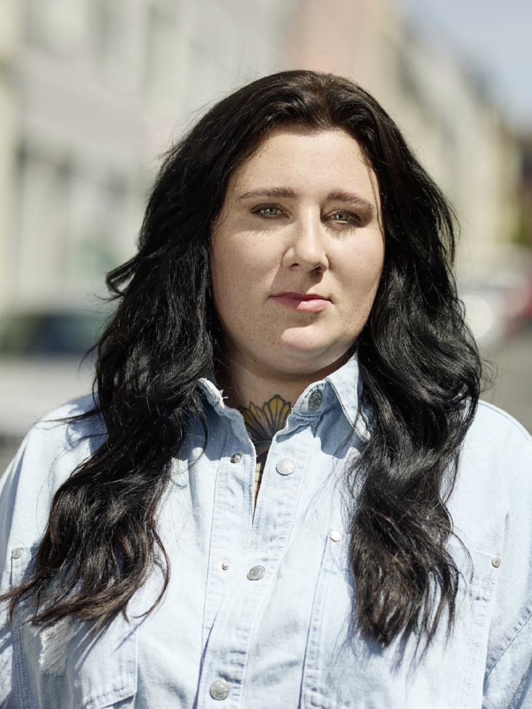 Porträt von Lena Schätte. Sie hat langes, welliges schwarzes Haar und trägt ein Jeanshemd.