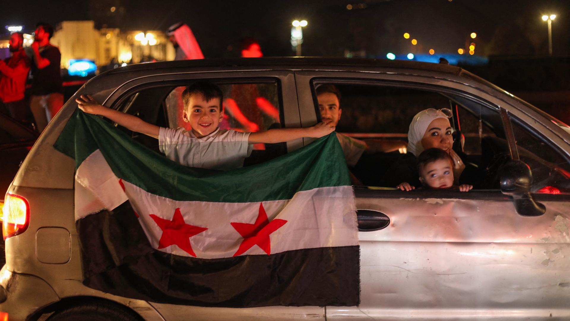 Damaskus, Syrien: Eine Familie sitzt in ihrem Auto. Auf der Rückbank beugt sich ein kleiner Junge durch das geöffnete Fenster und hält die syrische Flagge in die Kamera. Damaskus, Syrien: Eine Familie sitzt in ihrem Auto. Auf der Rückbank beugt sich ein kleiner Junge durch das geöffnete Fenster und hält die syrische Flagge in die Kamera.