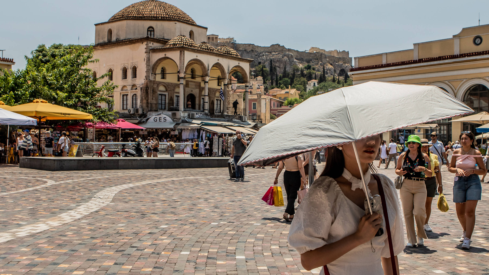 Eine Frau läuft durch die Straßen von der Stadt Athen und schützt sich mit einem Schirm vor der Sonne.