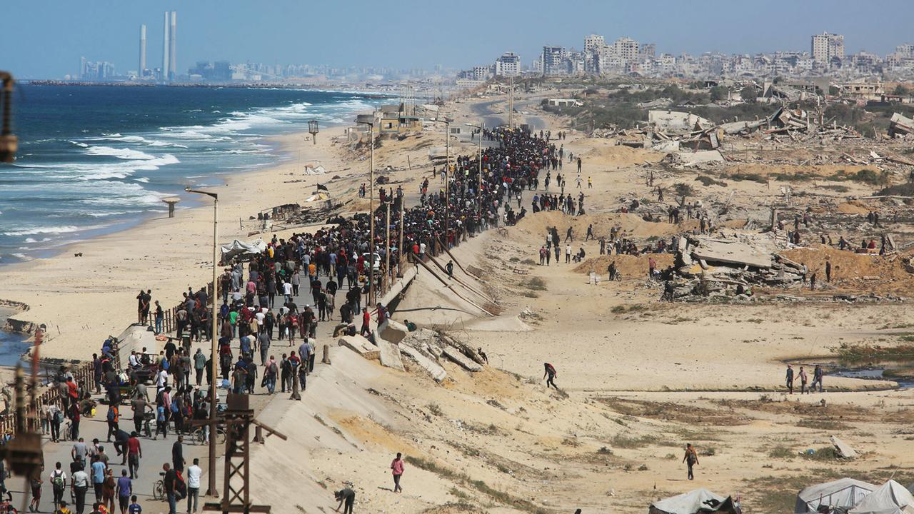Eine breite Schlange von Menschen läuft einen Standstreifen inmitten des zerstörten Gazastreifens, links das Meer, hinten Ruinen von Gaza-Stadt. Eine breite Schlange von Menschen läuft einen Standstreifen inmitten des zerstörten Gazastreifens, links das Meer, hinten Ruinen von Gaza-Stadt.