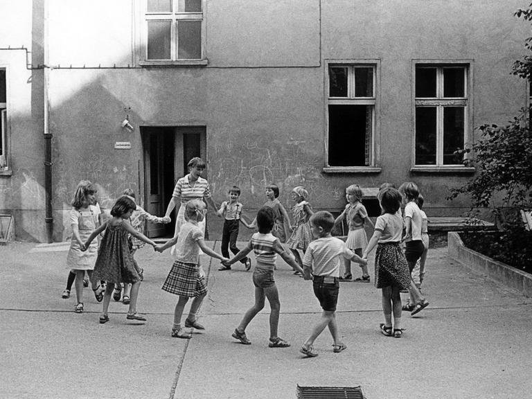 Kinder und ihre Erzieherin bei einem Kreisspiel im Hinterhof eines Kindergartens in Ostberlin, aufgenommen im März 1985.