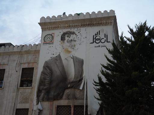 An einem Haus ein Bild von Assad, man sieht deutlich Kampfspuren und Einschusslöcher.