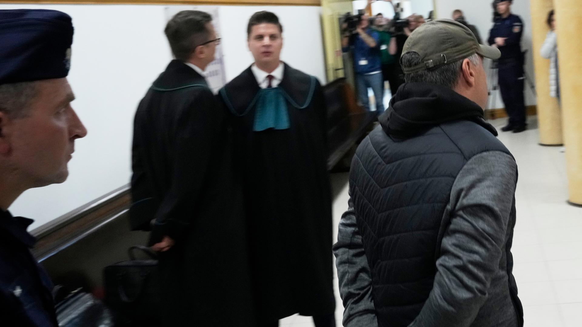 Ein Mann wird von einem Polizisten in einen Verhandlungsraum geführt. 