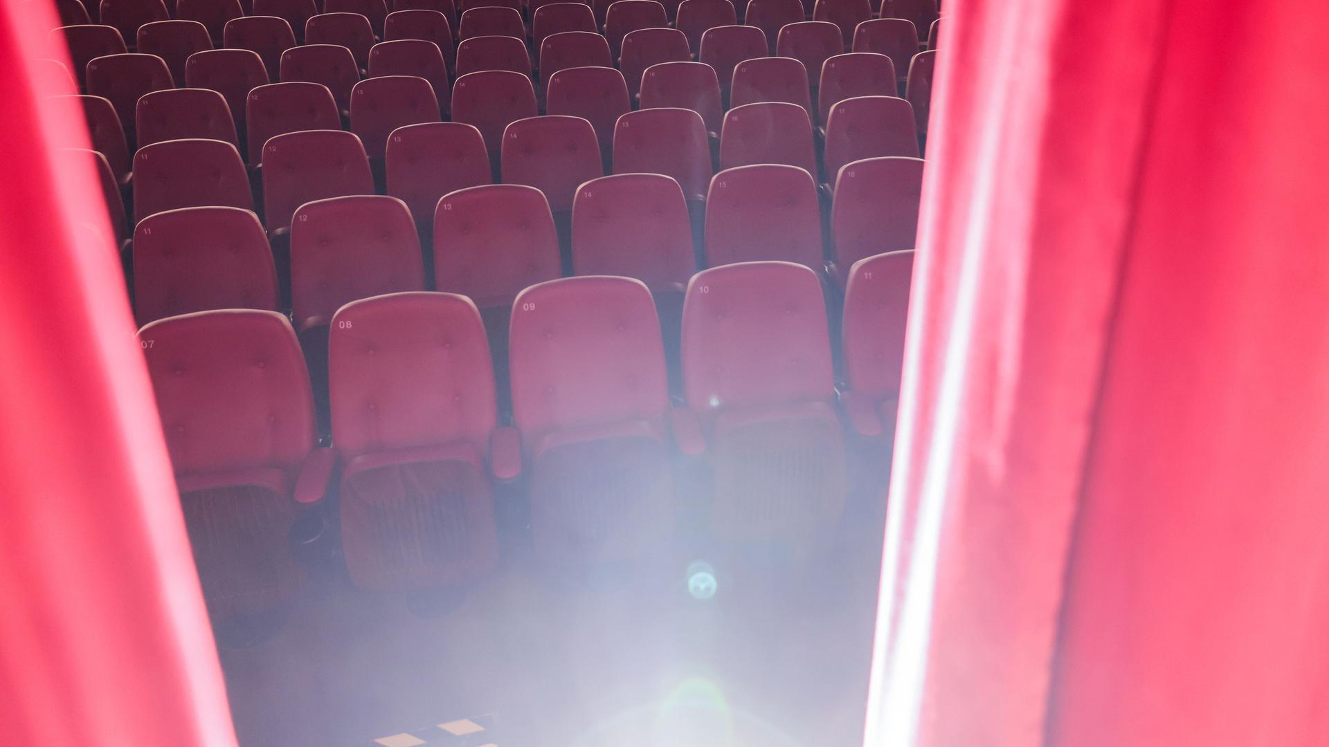 Ein roter Vorhang öffnet sich und gibt den Blick auf einen Saal mit leeren Kinosesseln frei. Ein roter Vorhang öffnet sich und gibt den Blick auf einen Saal mit leeren Kinosesseln frei.
