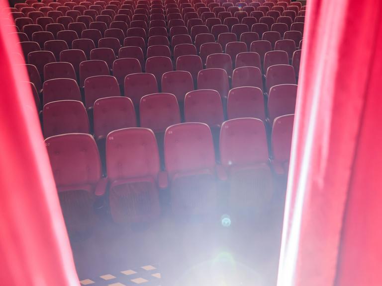 Ein roter Vorhang öffnet sich und gibt den Blick auf einen Saal mit leeren Kinosesseln frei.