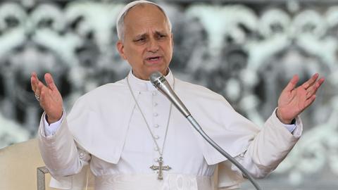 Papst Leo hat seine Arme ausgebreitet und spricht in ein Mikrofon.