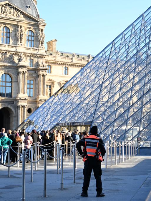 Menschen stehen Schlange, um das Louvre-Museum zu betreten. Im Pariser Louvre muss wegen baufälliger Fußböden ein Ausstellungsbereich vorsorglich und unerwartet für Besucher geschlossen werden. 