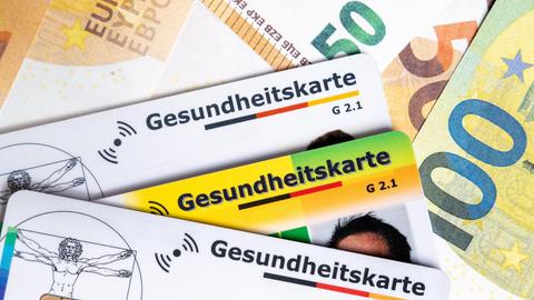 Mehrere Gesundheitskarten liegen auf Euroscheinen. Das Bild symbolisiert steigende Krankenkassenbeiträge, hohe Gesundheitskosten und die politische Debatte um die Finanzierung des Gesundheitssystems. 