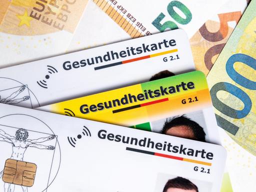 Mehrere Gesundheitskarten liegen auf Euroscheinen. Das Bild symbolisiert steigende Krankenkassenbeiträge, hohe Gesundheitskosten und die politische Debatte um die Finanzierung des Gesundheitssystems. Mehrere Gesundheitskarten liegen auf Euroscheinen. Das Bild symbolisiert steigende Krankenkassenbeiträge, hohe Gesundheitskosten und die politische Debatte um die Finanzierung des Gesundheitssystems.