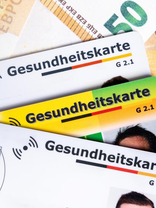 Mehrere Gesundheitskarten liegen auf Euroscheinen. Das Bild symbolisiert steigende Krankenkassenbeiträge, hohe Gesundheitskosten und die politische Debatte um die Finanzierung des Gesundheitssystems. Mehrere Gesundheitskarten liegen auf Euroscheinen. Das Bild symbolisiert steigende Krankenkassenbeiträge, hohe Gesundheitskosten und die politische Debatte um die Finanzierung des Gesundheitssystems.