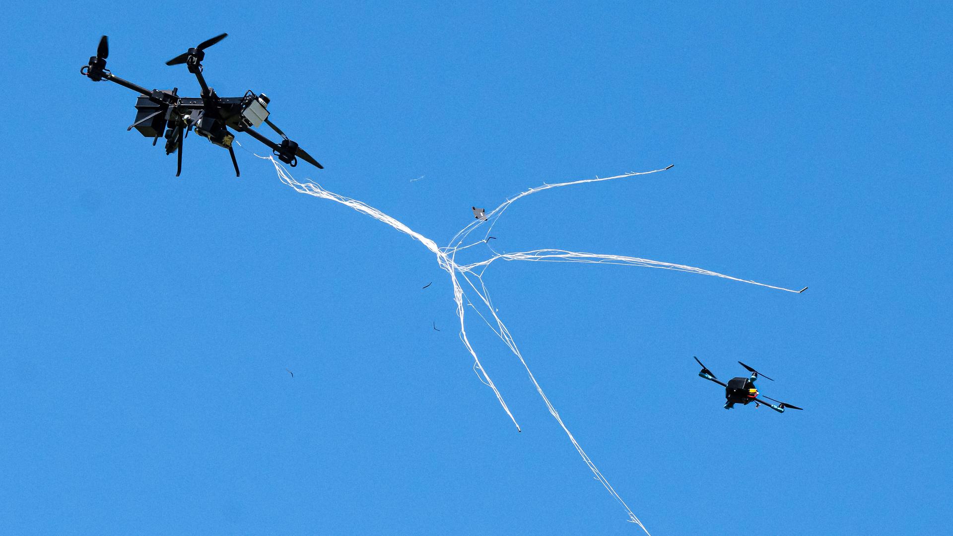 Eine Abfangdrohne schwebt durch die Luft und wirft ein Netz aus, um damit eine kleinere Drohne abzufangen. Eine Abfangdrohne schwebt durch die Luft und wirft ein Netz aus, um damit eine kleinere Drohne abzufangen.