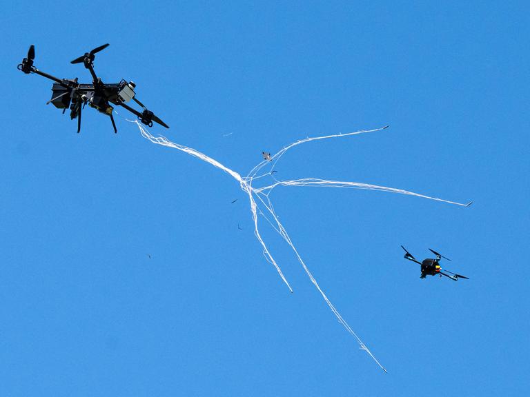 Eine Abfangdrohne schwebt durch die Luft und wirft ein Netz aus, um damit eine kleinere Drohne abzufangen.