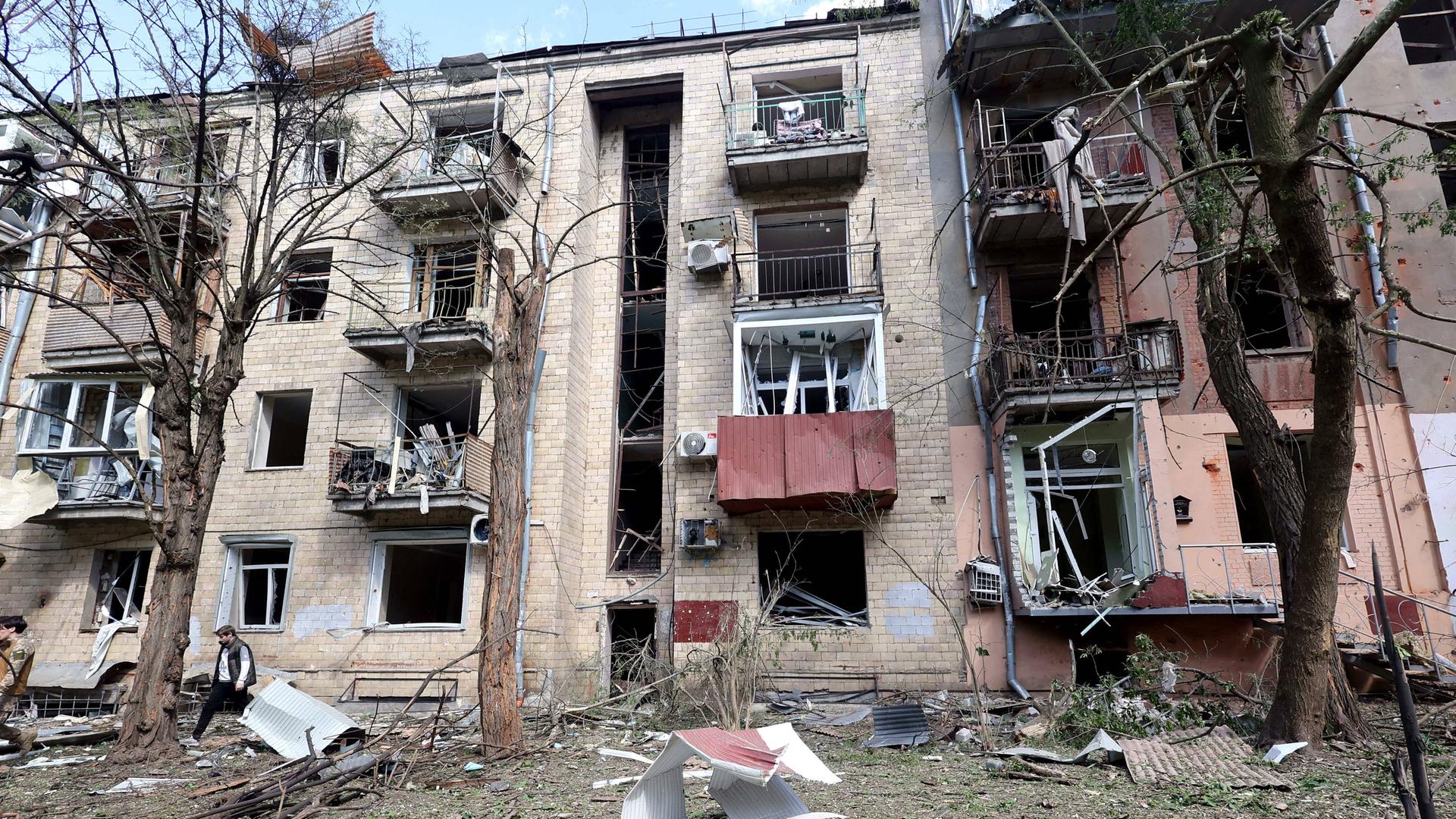 Ein beschädigter Wohnblock, die Fassade bröckelt an mehreren Stellen und Trümmerteile liegen vor dem Gebäude.