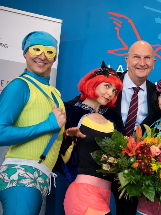 Trashig als Superhelden kostümierte Leute nehmen eine Auszeichnung entgegen und posieren dabei albern.