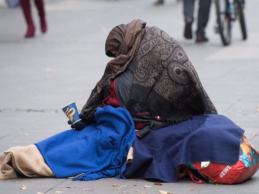 Eingehüllt in Decken bettelt eine Frau in einer Fussgängerzone in Frankfurt am Main um Kleingeld. 