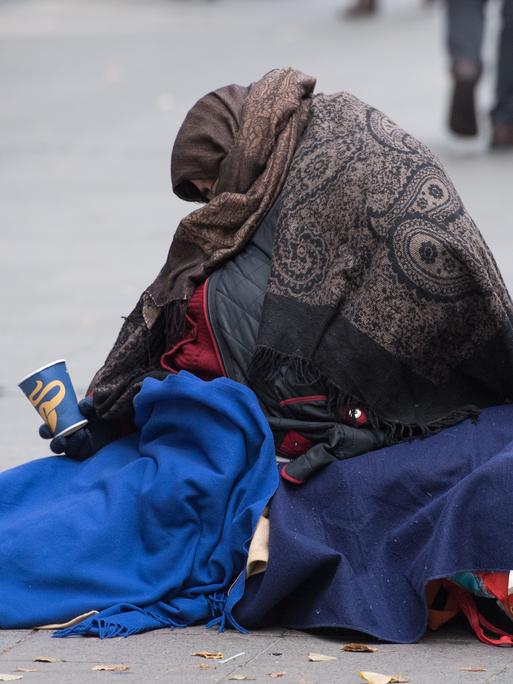 Eingehüllt in Decken bettelt eine Frau in einer Fussgängerzone in Frankfurt am Main um Kleingeld. 