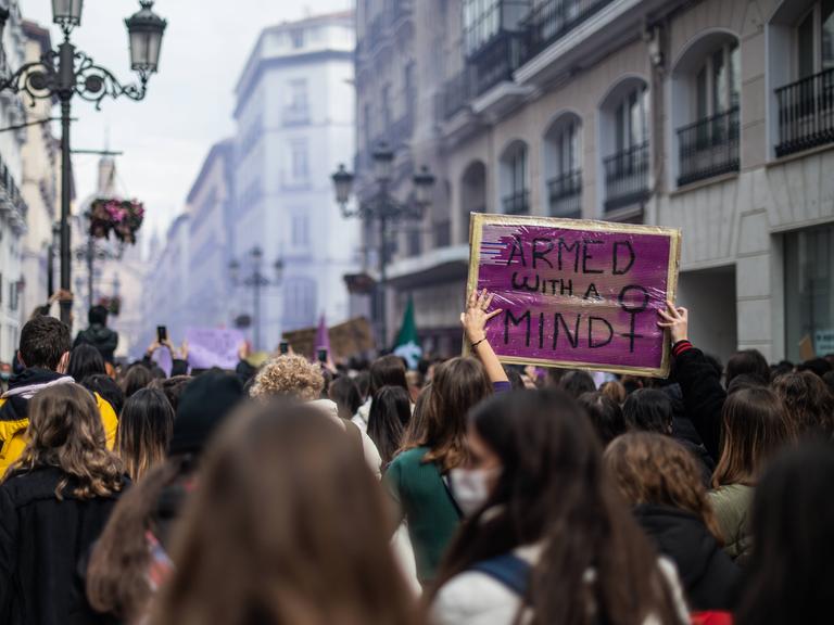 Bei einer feministischen Demonstration ist ein Plakat mit der Aufschrift "Armed With A Mind" zu sehen.