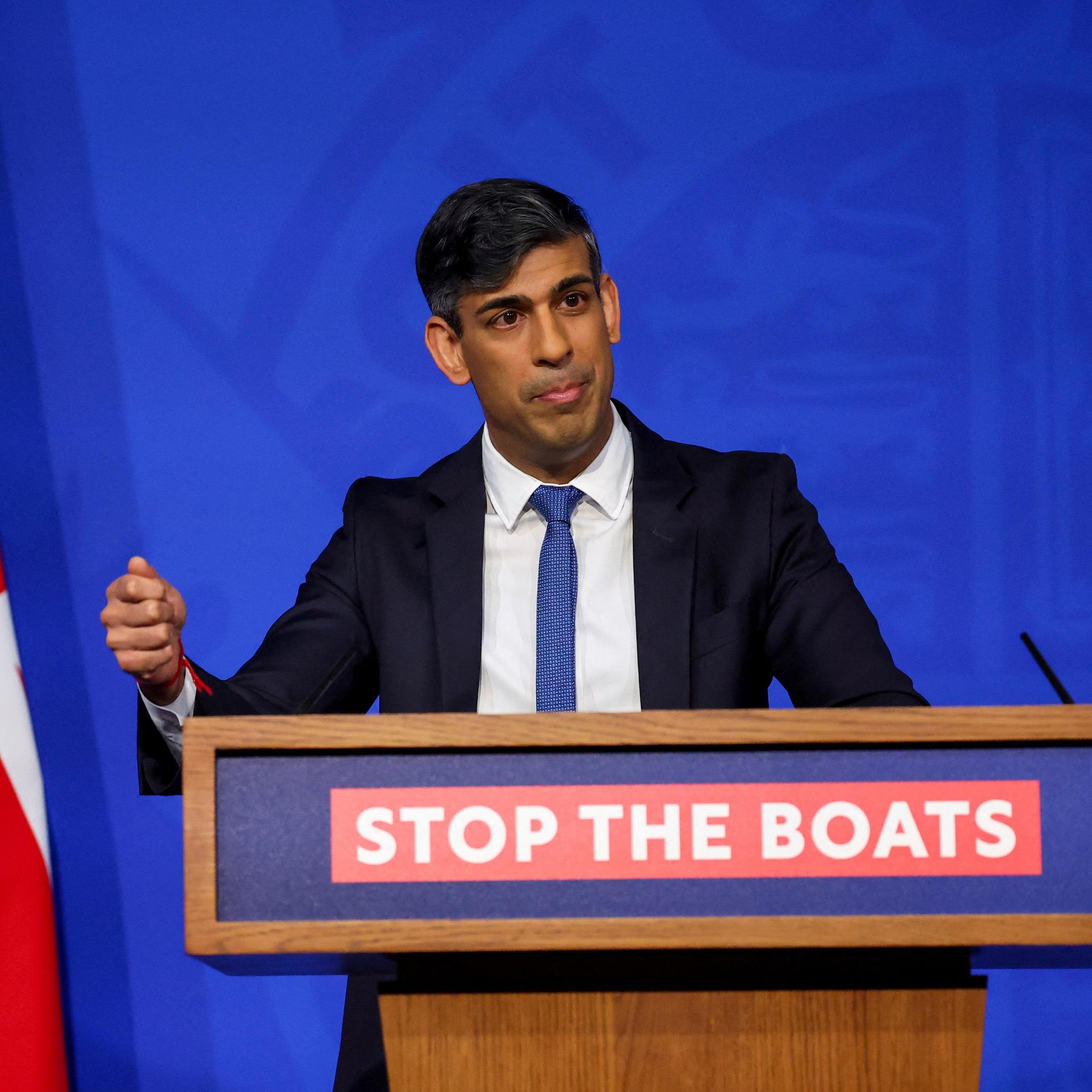 Sunak steht bei einer Pressekonferenz hinter einem Rednerpult. Im Hintergrund ist die britische Flagge zu sehen. 