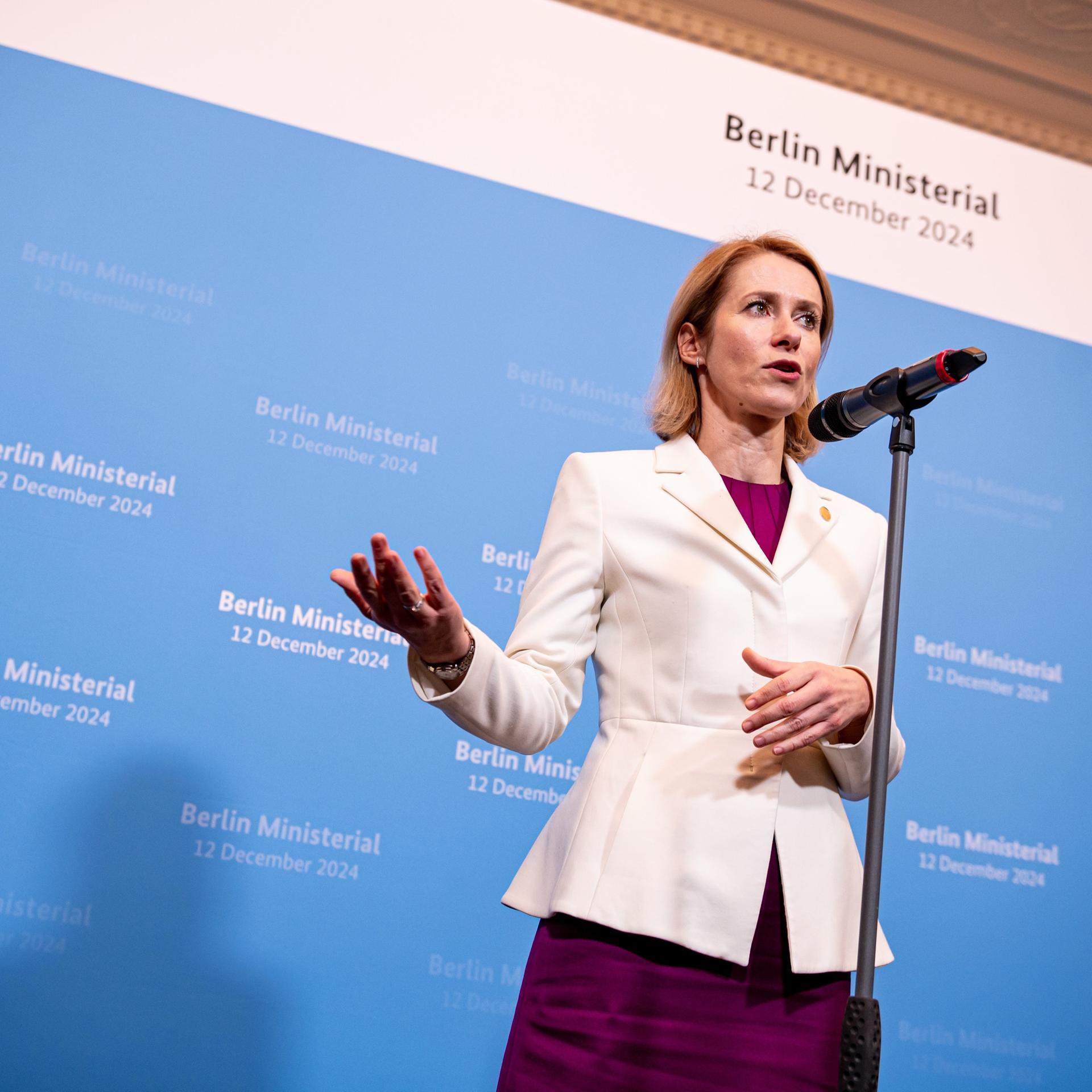 Eine Frau steht vor einem blauen Hintergrund und spricht in ein Mikrofon.