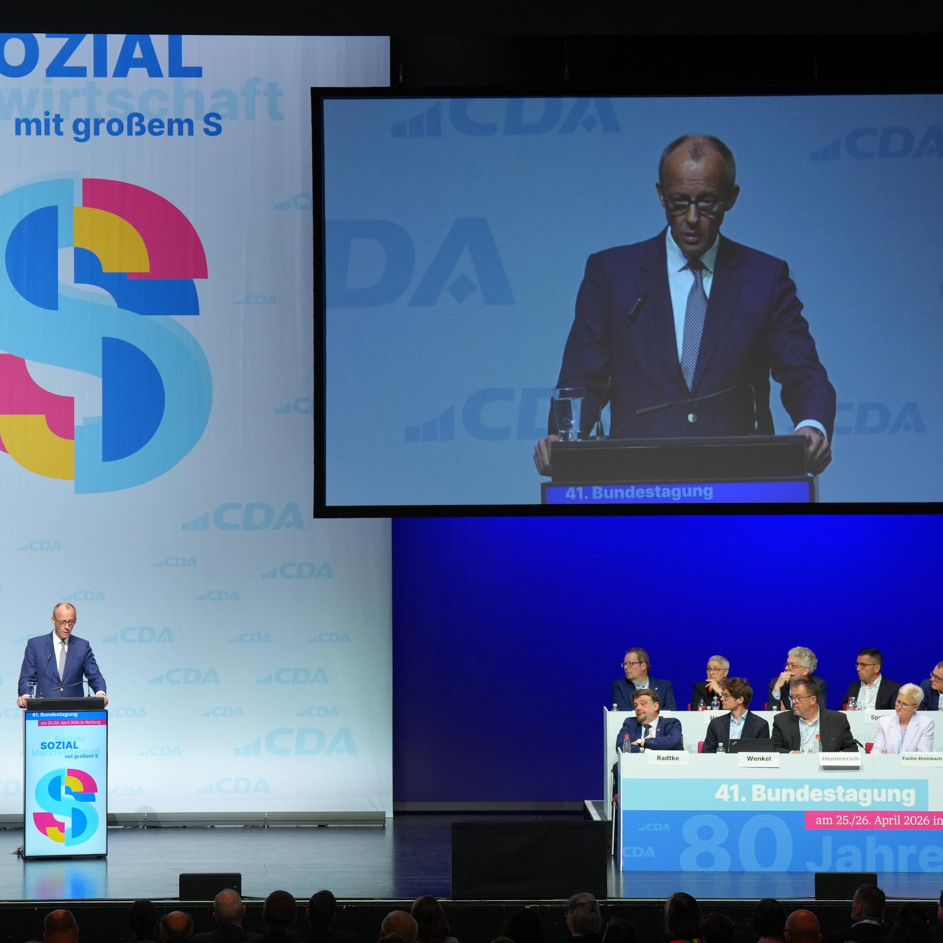Bundeskanzler Merz steht auf einer Bühne und spricht bei der 41. Bundestagung der Christlich-Demokratische Arbeitnehmerschaft (CDA) in Marburg. Im Hintergrund wird seine Rede auf einer großen Leinwand übertragen.