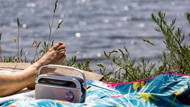 Ein Radio steht am auf einer Picknickdecke, auf der eine Person am Senftenberger See in der Sonne liegt.