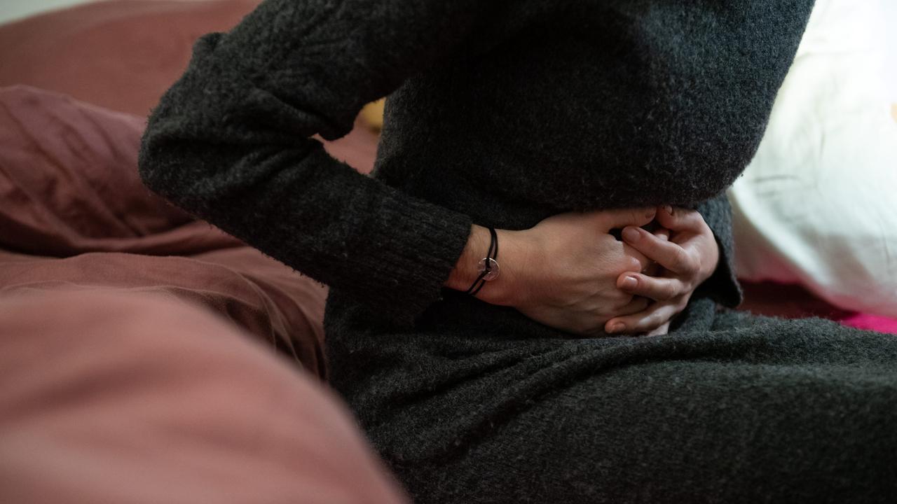 Eine Frau sitzt auf der Couch und hält sich den Bauch.