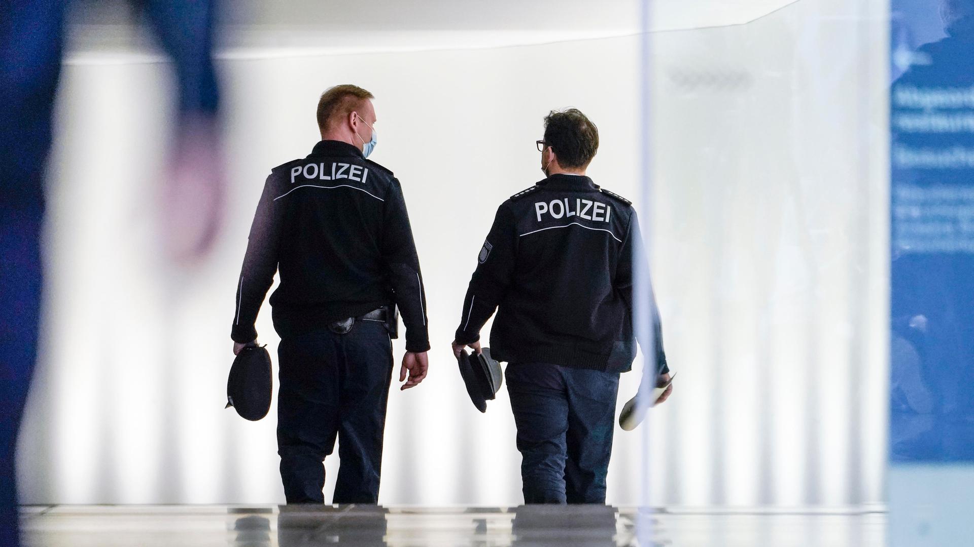 Einsatzbeamte der Polizei laufen in einem Gebäude die Treppe herunter. Die beiden Männer sind von hinten zu sehen.