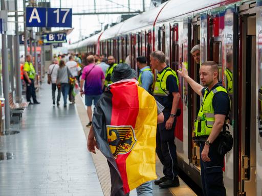 Sicherheitspersonal der Bahn weist einem deutschen Fan den Weg zu einem freien Abteil, ganz am Ende des Zuges. 