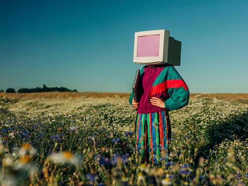 Person mit Monitor-Kopf im Trainingsanzug der 90er auf einer Sommerwiese Person mit Monitor-Kopf im Trainingsanzug der 90er auf einer Sommerwiese