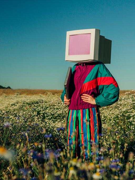 Person mit Monitor-Kopf im Trainingsanzug der 90er auf einer Sommerwiese Person mit Monitor-Kopf im Trainingsanzug der 90er auf einer Sommerwiese