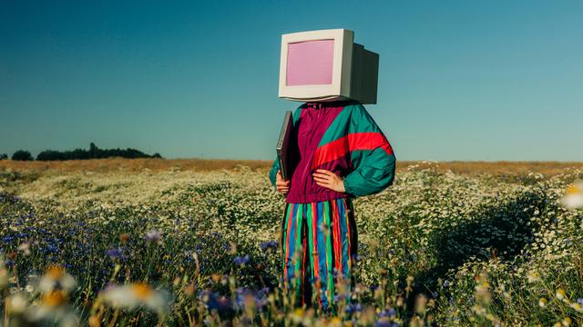 Person mit Monitor-Kopf im Trainingsanzug der 90er auf einer Sommerwiese