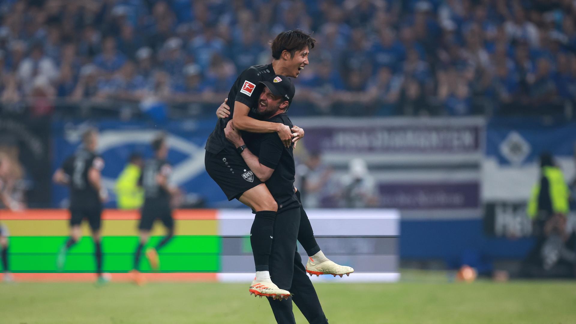 Iwata springt an Hoensß hoch, der ihn umarmt. Im Hintergrund unscharf weitere feiernde Stuttgarter und eine eine vollbesetzte Tribüne.