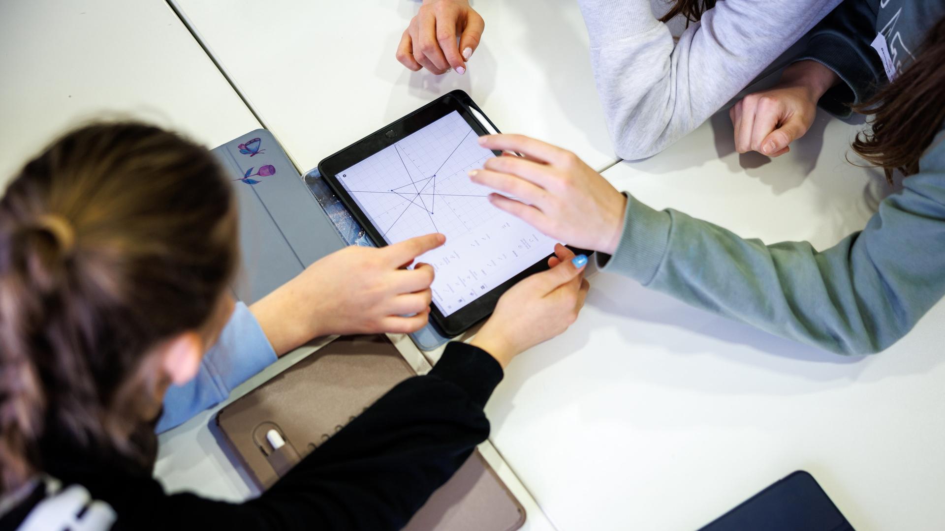 Schülerinnen einer siebten Klasse arbeiten in einem Klassenraum in einer Unterrichtsstunde im Fach Mathe gemeinsam an einem Tablet. 