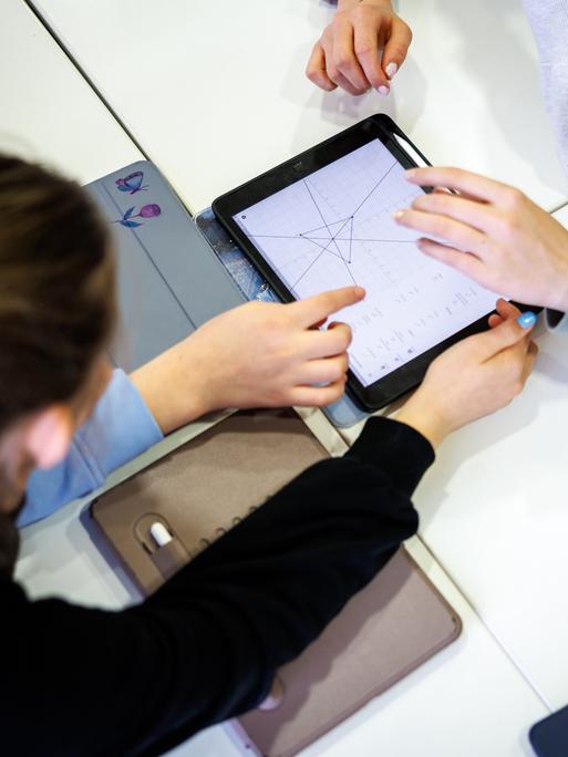 Schülerinnen einer siebten Klasse arbeiten in einem Klassenraum in einer Unterrichtsstunde im Fach Mathe gemeinsam an einem Tablet.  Schülerinnen einer siebten Klasse arbeiten in einem Klassenraum in einer Unterrichtsstunde im Fach Mathe gemeinsam an einem Tablet.