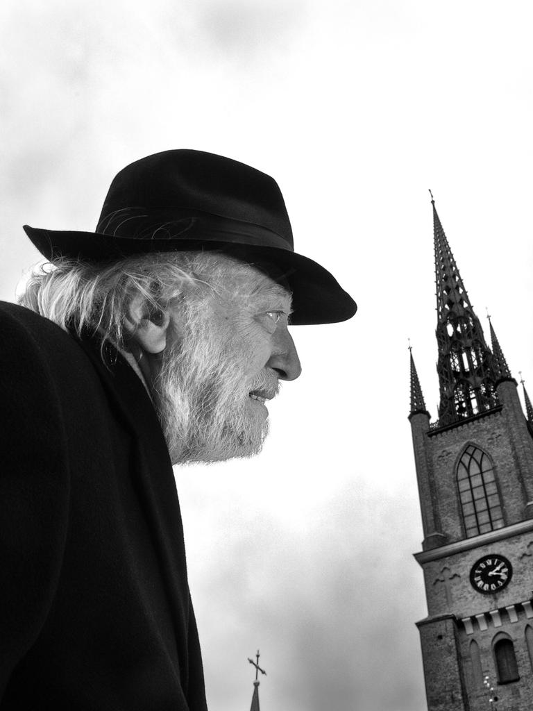 Autor László Krasznahorkai auf einem schwarz-weiß Bild in gebückter Haltung und mit Hut. Rechts daneben sieht man einen alten Kirchturm.