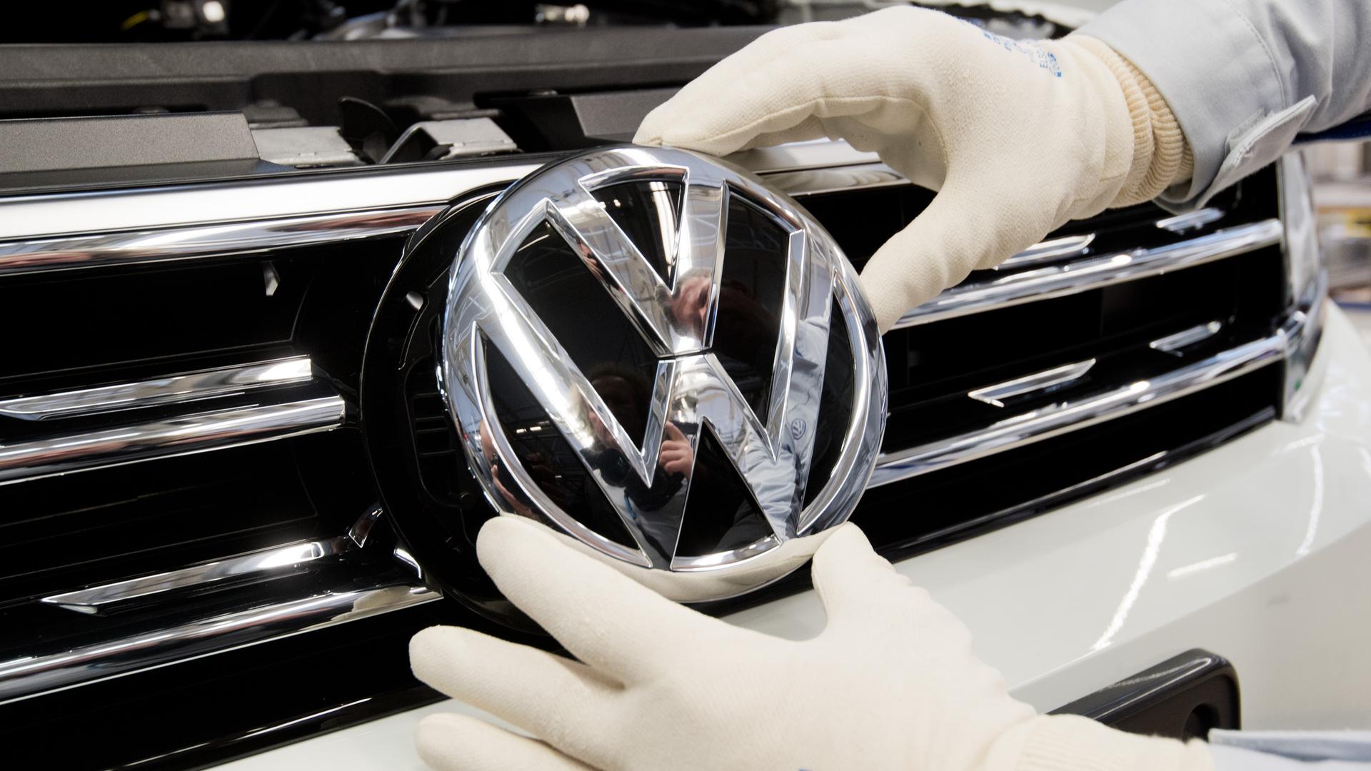 Ein Mitarbeiter montiert ein VW Logo an die Front eines VW Tiguan 