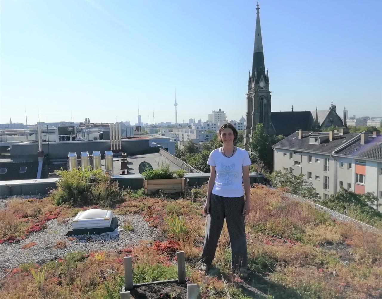 Eine Frau steht auf einem begrünten Hausdach in Berlin. 