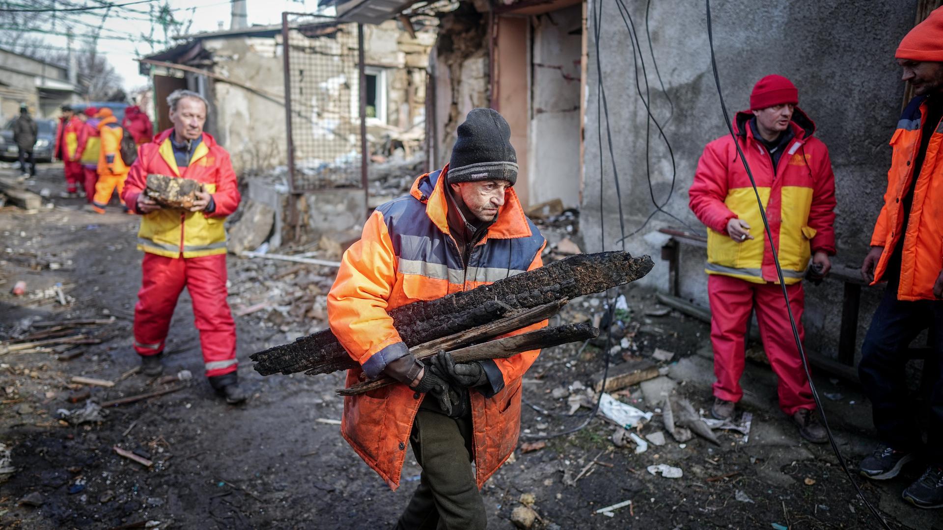 Helfer beseitigen nach einem nächtlichen Drohnenangriff am Morgen die Trümmer in der Hafenstadt Odessa. Die Männer in orangenen Jacken tragen Trümmerteile.