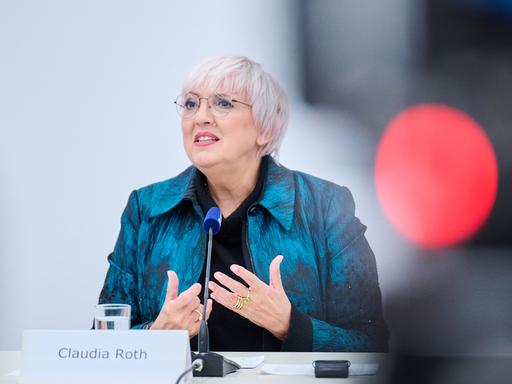 Claudia Roth. Eine ältere Frau mit kurzen hellen Haaren und Brille steht an einem Pult und hält eine Rede.