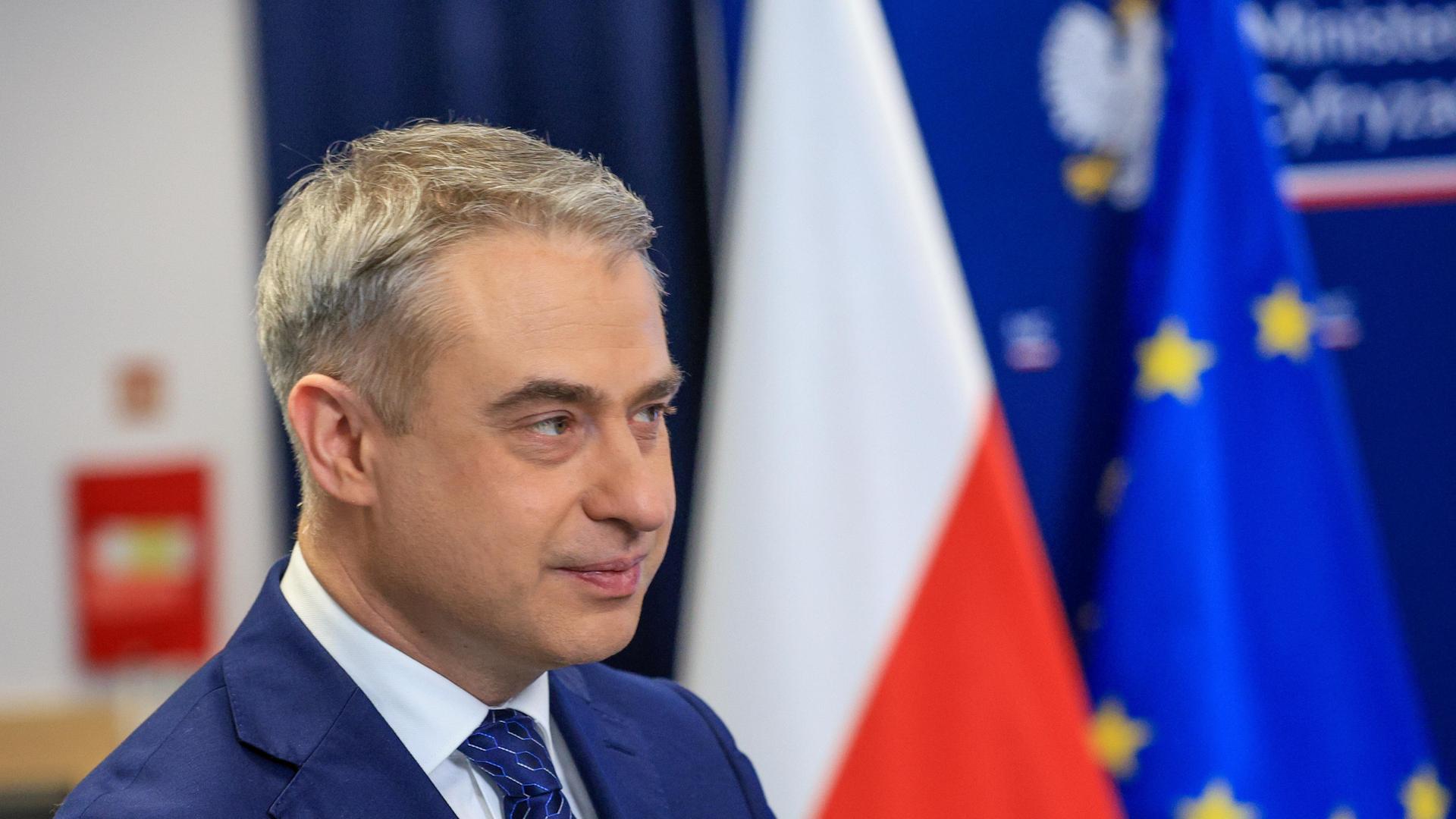 Polens Digitalminister Krzysztof Gawkowski von der Seite. Hinter ihm sind die polnische und europäische Flaggen leicht verschwommen. 