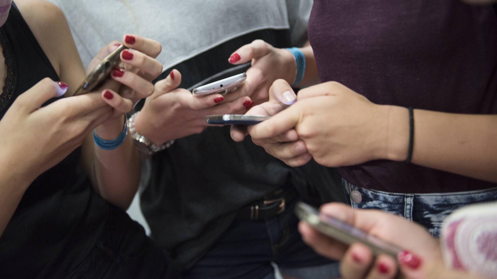 Man sieht die Hände mehrerer Mädchen. Sie halten jeder ein Smarphone in der Hand und tippen darauf. Man sieht die Hände mehrerer Mädchen. Sie halten jeder ein Smarphone in der Hand und tippen darauf.